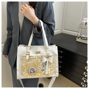 Close-up of a white Ita bag with clear window, yellow lace trim, and ribbon accessories