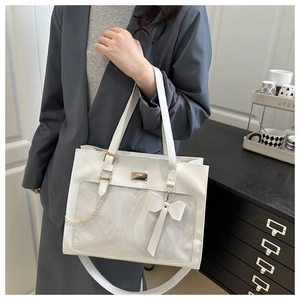 Close-up of white tote bag with clear window, decorative bow and gold chain details