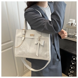Detail of white tote bag featuring transparent PVC window and golden chain bow ornament