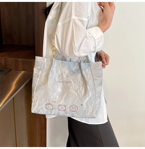 Detail of a textured silver tote bag with bear print and metal chain shoulder strap
