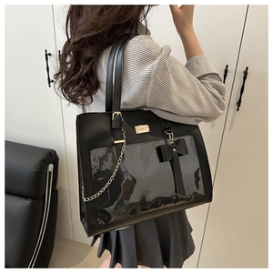 Detail of a black leather ita bag featuring a large clear window and a ribbon bow charm
