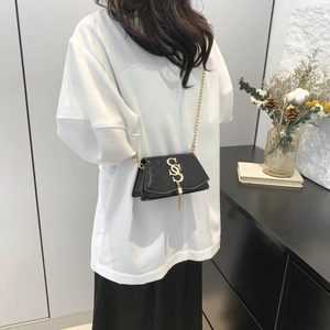 Glänzende schwarze Mini-Klappentasche mit Goldlogo und Quastenkette am Modell
