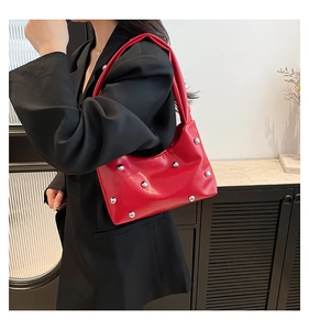 Close-up of vibrant red leather shoulder bag featuring silver stud details on a model