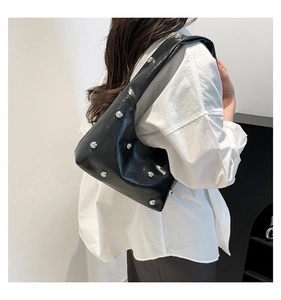 Detail of black glossy leather shoulder bag with silver studs worn by a model