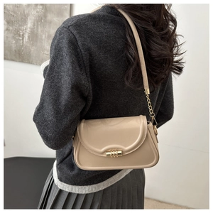 Detailed view of beige leather crossbody bag with gold lock on gray sweater outfit