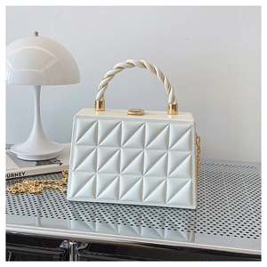 Detail of white quilted geometric handbag with gold chain strap and twisted handle