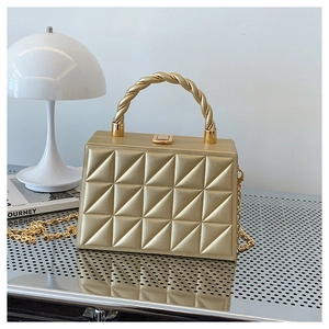 Close-up of golden embossed box bag with quilted texture and twisted rope handle
