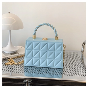 Detail of light blue quilted box bag with spiral top handle and gold chain strap