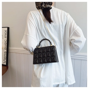 Detailed shot of a black quilted leather box bag featuring a woven handle and gold chain