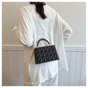 Detail of black quilted box bag with woven handle and gold chain strap on model