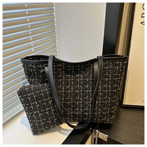 Detail of tweed tote bag with matching pouch and black leather trims on dark surface