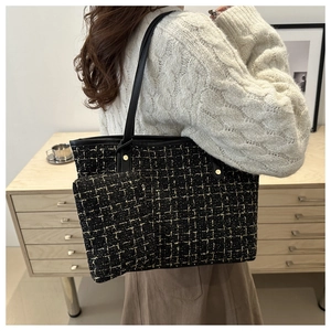 Detail of black and gold tweed tote bag with leather strap worn on white sweater