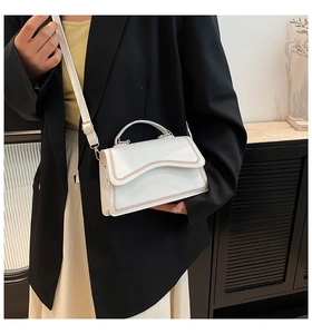 White leather handbag with brown wavy stitching and gold buckle shown in a lifestyle setting
