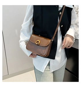 Brown vintage square crossbody bag worn by model over a white shirt and black vest