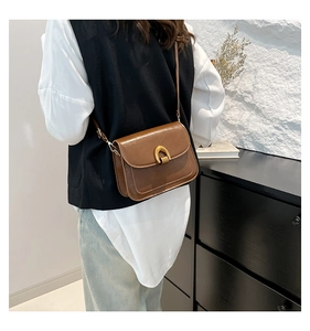 Detail of dark brown leather crossbody bag with a prominent golden U-shaped metal buckle