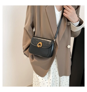 Detail of black crossbody bag with gold U-shaped buckle on classic professional outfit