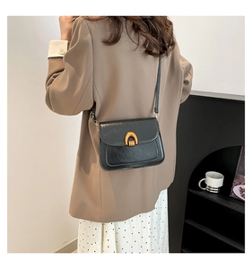 Detail of a black textured leather crossbody bag with a vintage gold horseshoe buckle