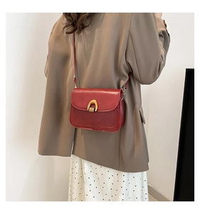 Detail of burgundy leather saddle bag with golden U-shaped hardware on a model