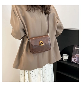 Detail of vintage dark brown crossbody bag with u-shaped gold buckle and glossy finish