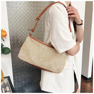 Detailed view of a woven straw shoulder bag with brown leather strap worn by a model