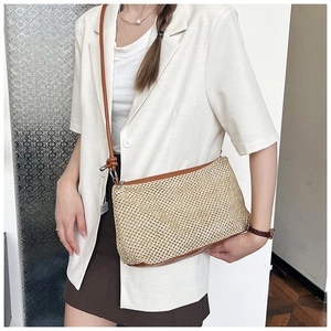Detail of handwoven straw crossbody bag with brown leather trim and slim shoulder strap