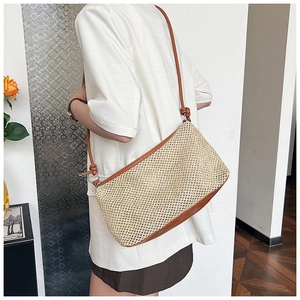 Side view of a large woven straw tote bag with brown leather straps worn by a model