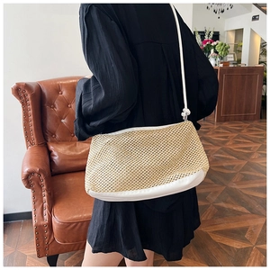 Straw knit crossbody bag with white leather trim shown on shoulder in a vintage room