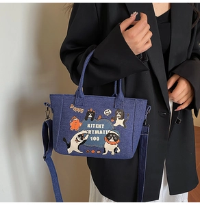 Detail of blue denim tote bag featuring cartoon cat prints and adjustable shoulder strap