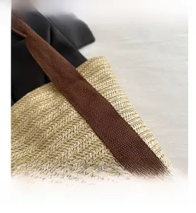 Close-up of the woven straw texture and brown canvas shoulder strap of the tote bag