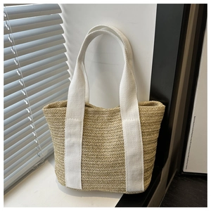 Detail of woven straw tote bag featuring herringbone texture and white fabric straps