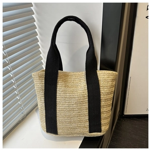 Detail view of woven straw tote bag texture and black canvas straps on white windowsill