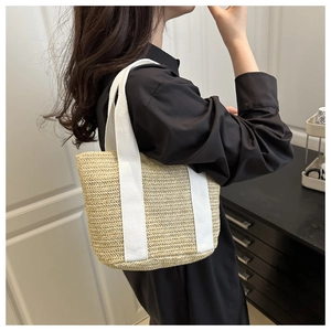 Detail of hand-woven straw tote with white canvas straps shown on model's shoulder