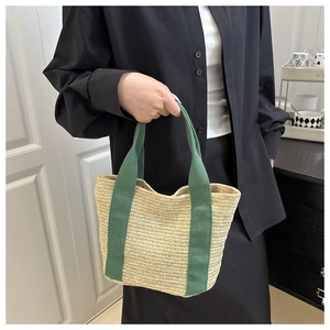Detail of straw woven tote bag featuring dark green fabric handles and natural texture