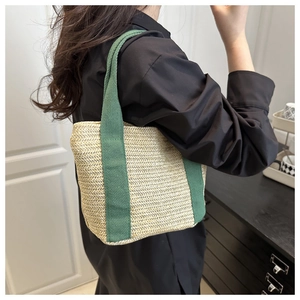 Detail of hand-woven straw tote bag with green canvas handles shown on a model