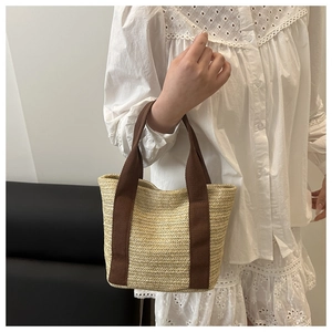 Detail of woven straw tote bag featuring contrast dark brown canvas straps and texture