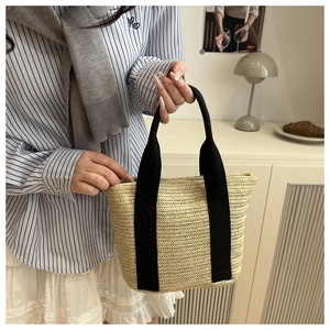 Detail of woven straw tote bag featuring wide black canvas handles and natural texture