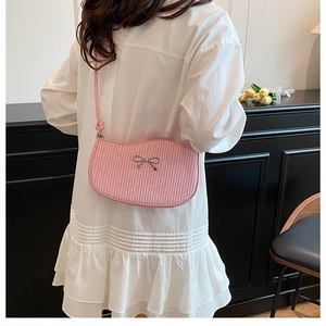 Pink woven crossbody bag detail featuring a silver bow accent and slim braided strap