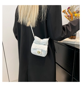 White quilted mini crossbody bag with a bow detail and gold chain strap on shoulder