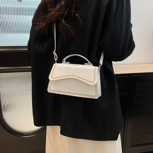 White minimalist crossbody bag with gold V-stitching on flap, shown on model's shoulder