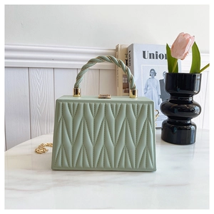Detail of green pleated box bag with spiral handle and gold chain on marble surface