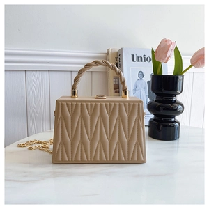 Detail of quilted leather handbag with spiral handle and gold chain on marble surface