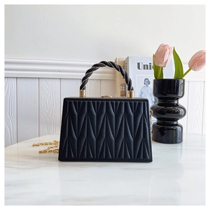 Detail of black pleated matelassé handbag with gold chain on white marble surface