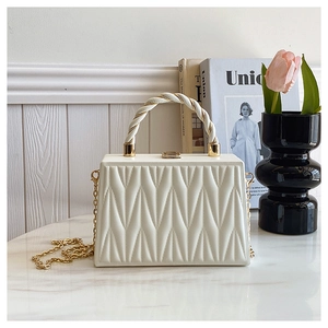 Detail view of cream quilted box bag with V-shaped stitching and golden chain strap