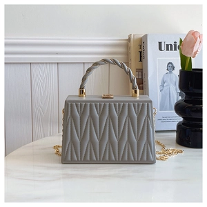 Detail of grey quilted crossbody bag with gold chain strap and woven handle on marble