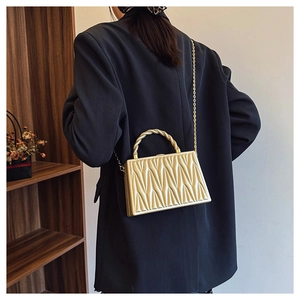 Detailed view of a gold metallic hard shell evening bag with V-quilted texture and chain