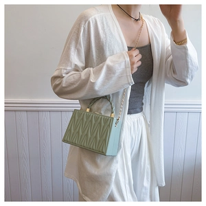 Detail of light green box bag with V-quilting, braided handle and gold chain strap