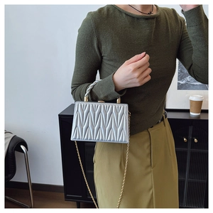 Close-up of silver quilted crossbody bag with golden chain strap and twisted handle