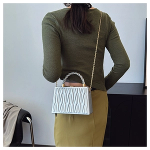 Detail of silver crossbody bag with pleated texture and metallic knotted handle worn by model