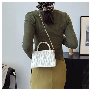 Detail of white quilted crossbody bag with golden chain and woven handle on model