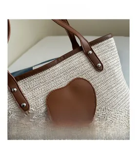 Détail d'un sac cabas en paille avec écusson cœur en cuir et rivets argentés discrets